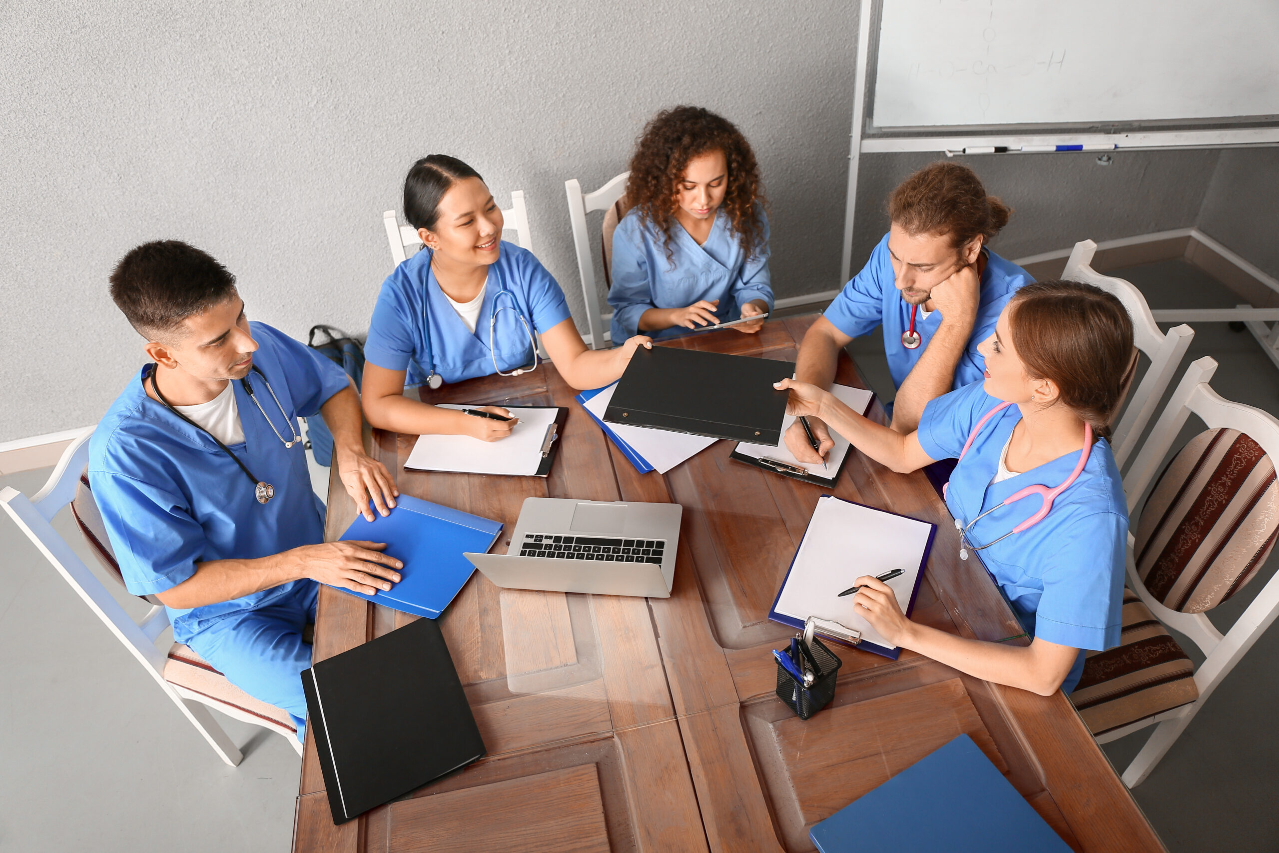 Group of health care professionals An overhead image of five health care professionals in blue scrubs sharing notes and resources around a table.