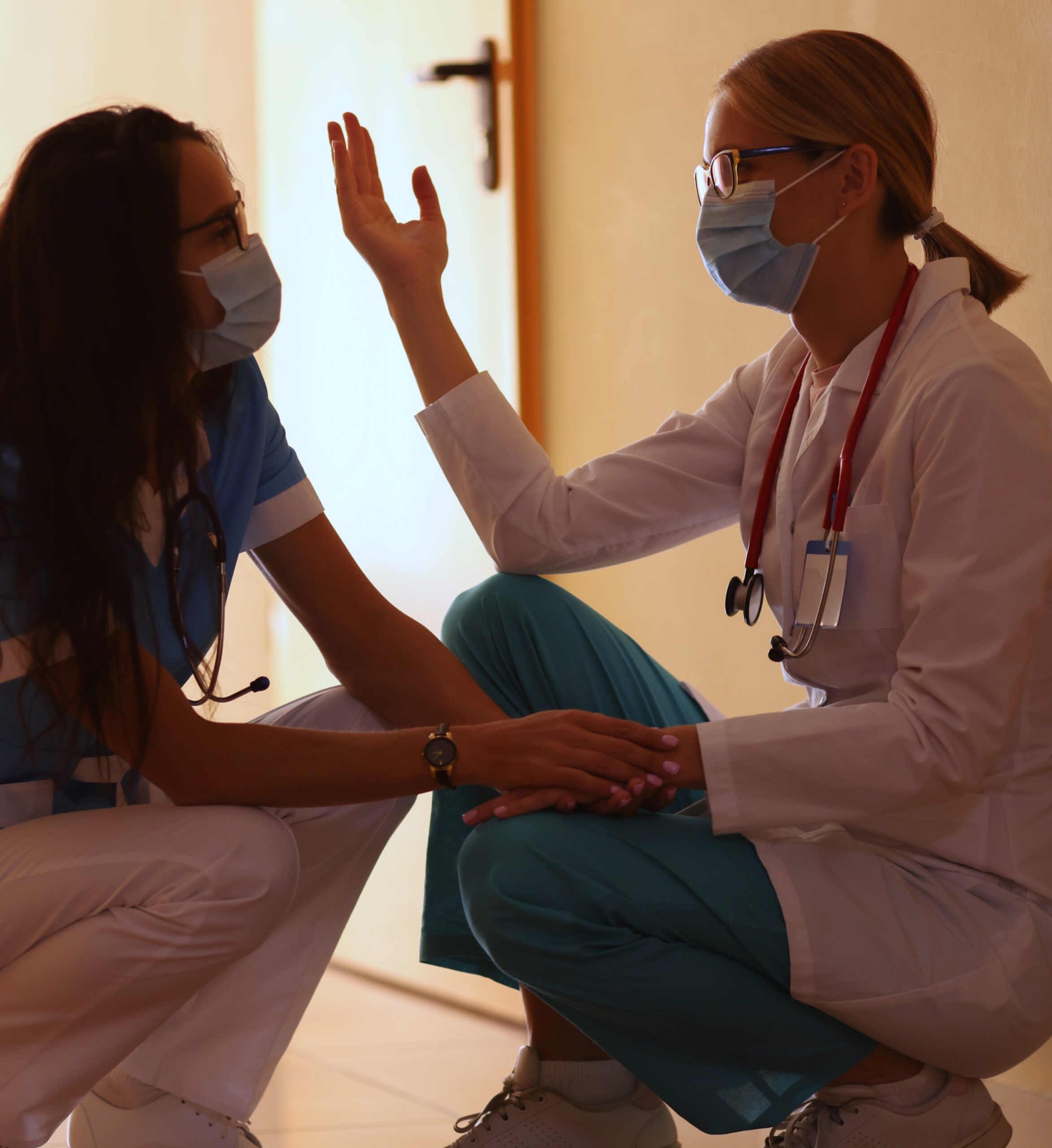 Two female doctors sitting in a hospital hallway discussing mental health challenges.
