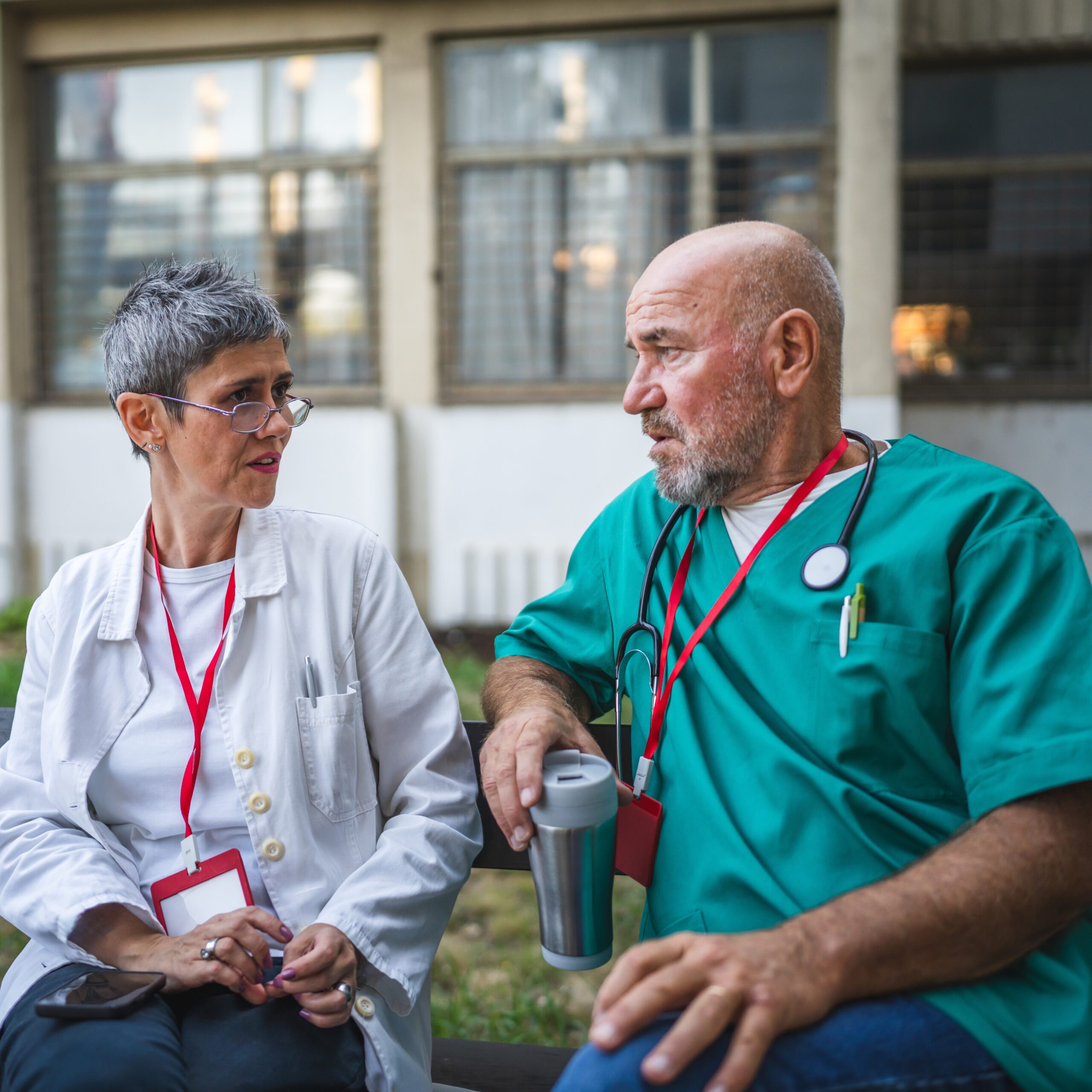 When To Reach Out For Health Care Professionals Two health care professionals having a conversation about mental health challenges on a quiet bench outside their building.